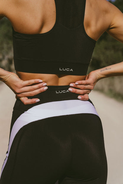 Close-up-back-view-of-a-woman- wearing-black-LUCA-cycling- including-a-mesh-racerback-sports- bra-and-high-waisted-leggings-with- thick-white-and-lavender-side- stripes-Premium-cycling-clothing- set