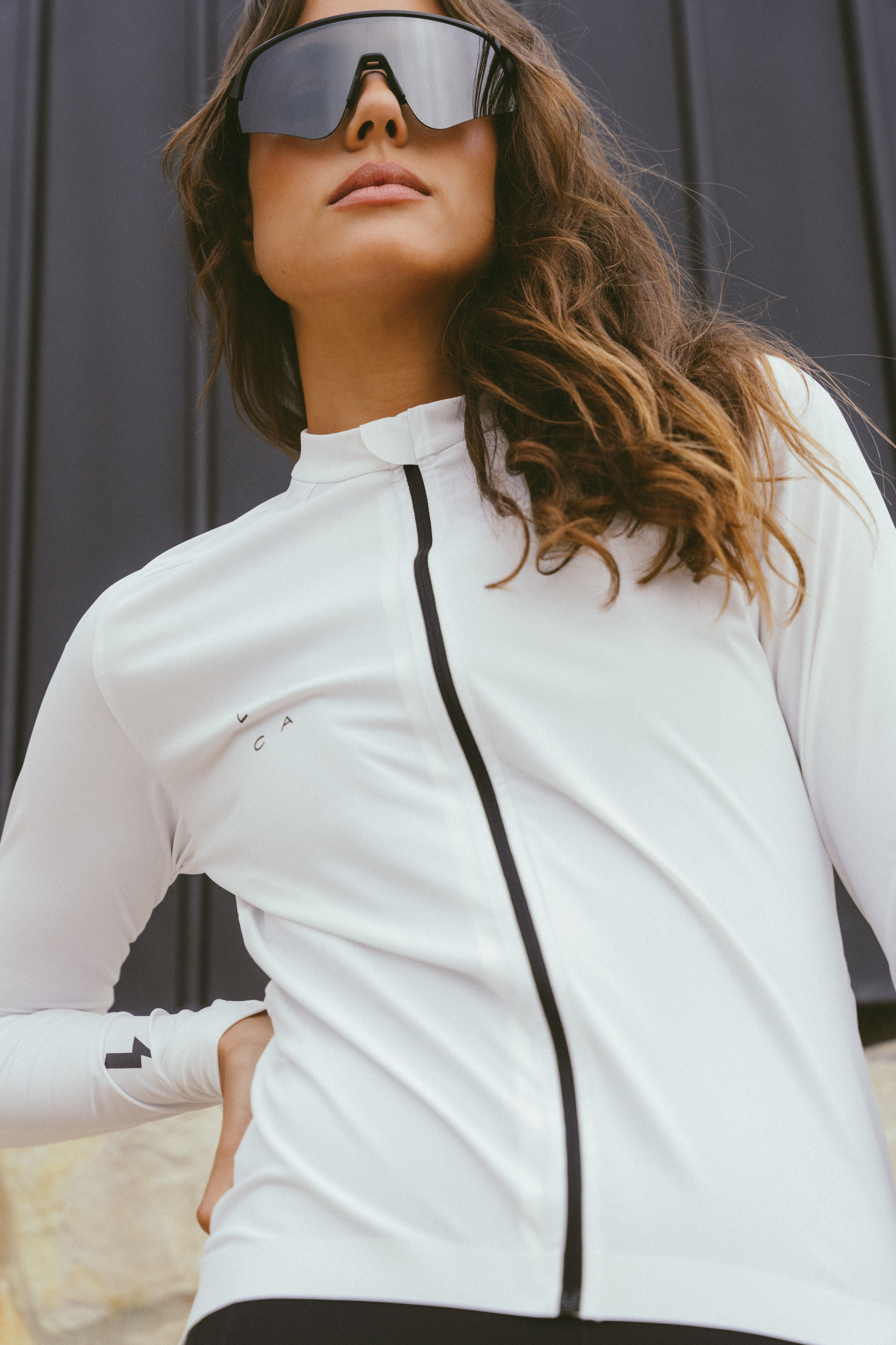 Dynamic-shot-of-a-model-wearing- large-black-mirrored-shield- sunglasses-and a Horizon Jersey - White-cycling-with-a-black- contrasting-zipper