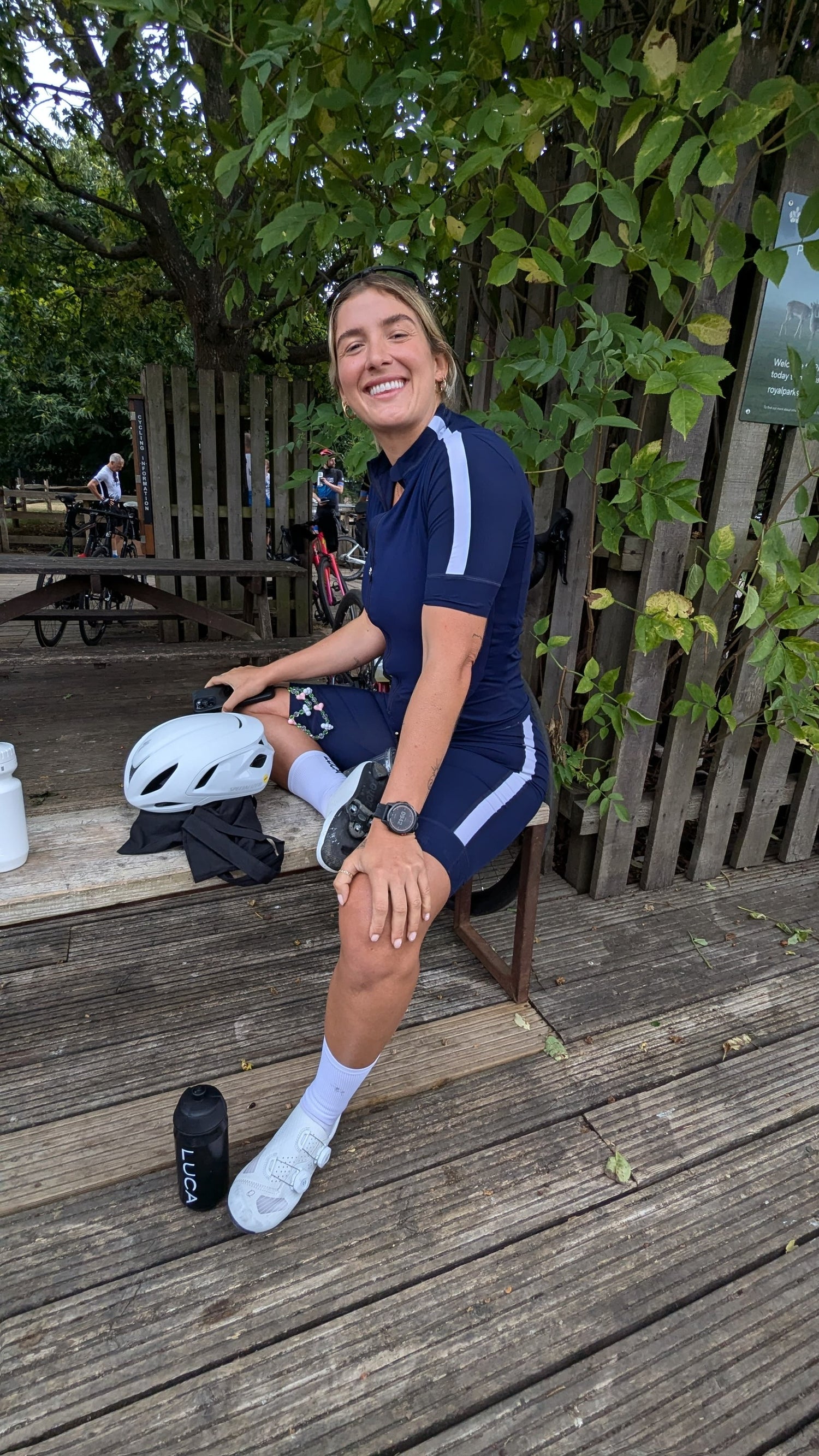 Smiling-female-cyclist-taking-a-rest- outdoors-wearing-a-dark-blue- cycling-jersey-and-shorts-set-with- white-stripes