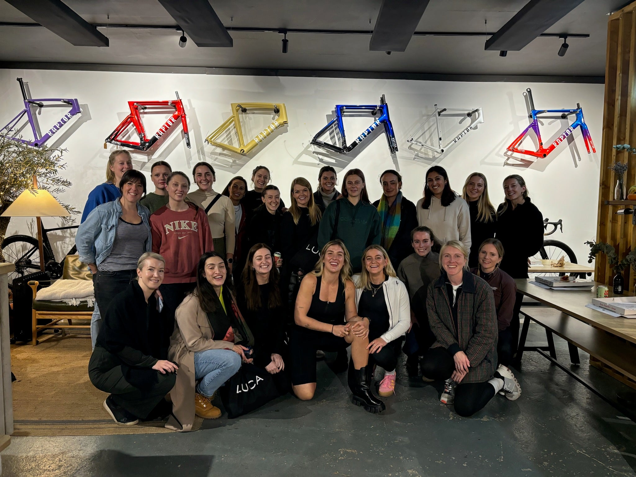 Large-group-of-women-posing-in- front-of-a-white-wall-decorated-with-colorful-bicycle-frames-in-a- stylish-indoor-space