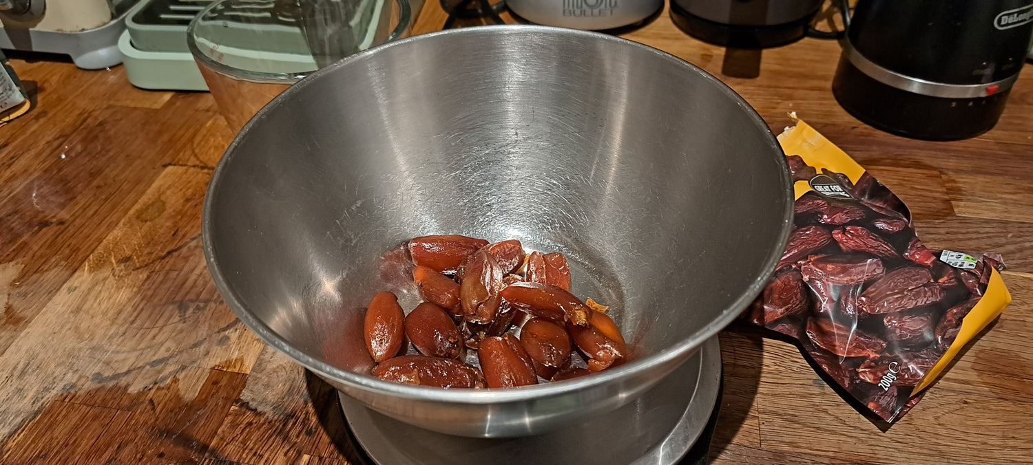 A-few-plump-dark-brown-dates- being-weighed-in-a-stainless-steel- kitchen-bowl-on-a-wooden-countertop-next-to-the-date- packaging