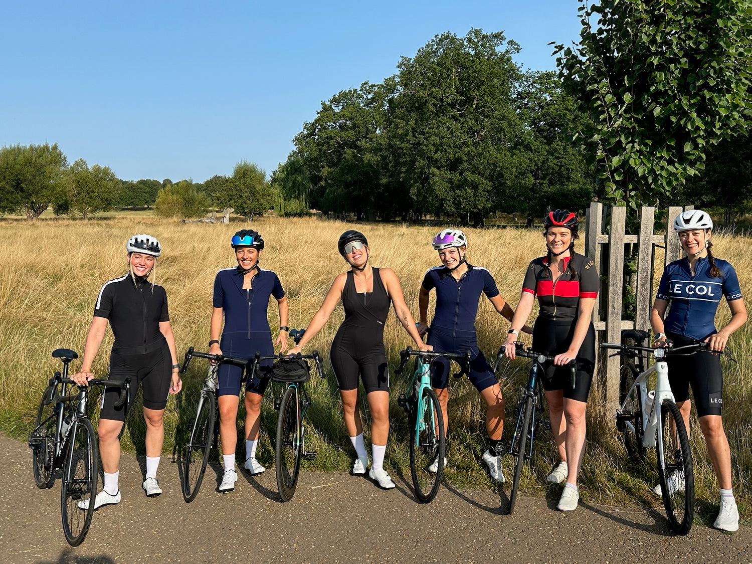 Outdoor-photo-of-a-women's-cycling-club-team=all-wearing- cycling-apparel-and-helmets-posing-with-their-bike-in-a-rural- setting