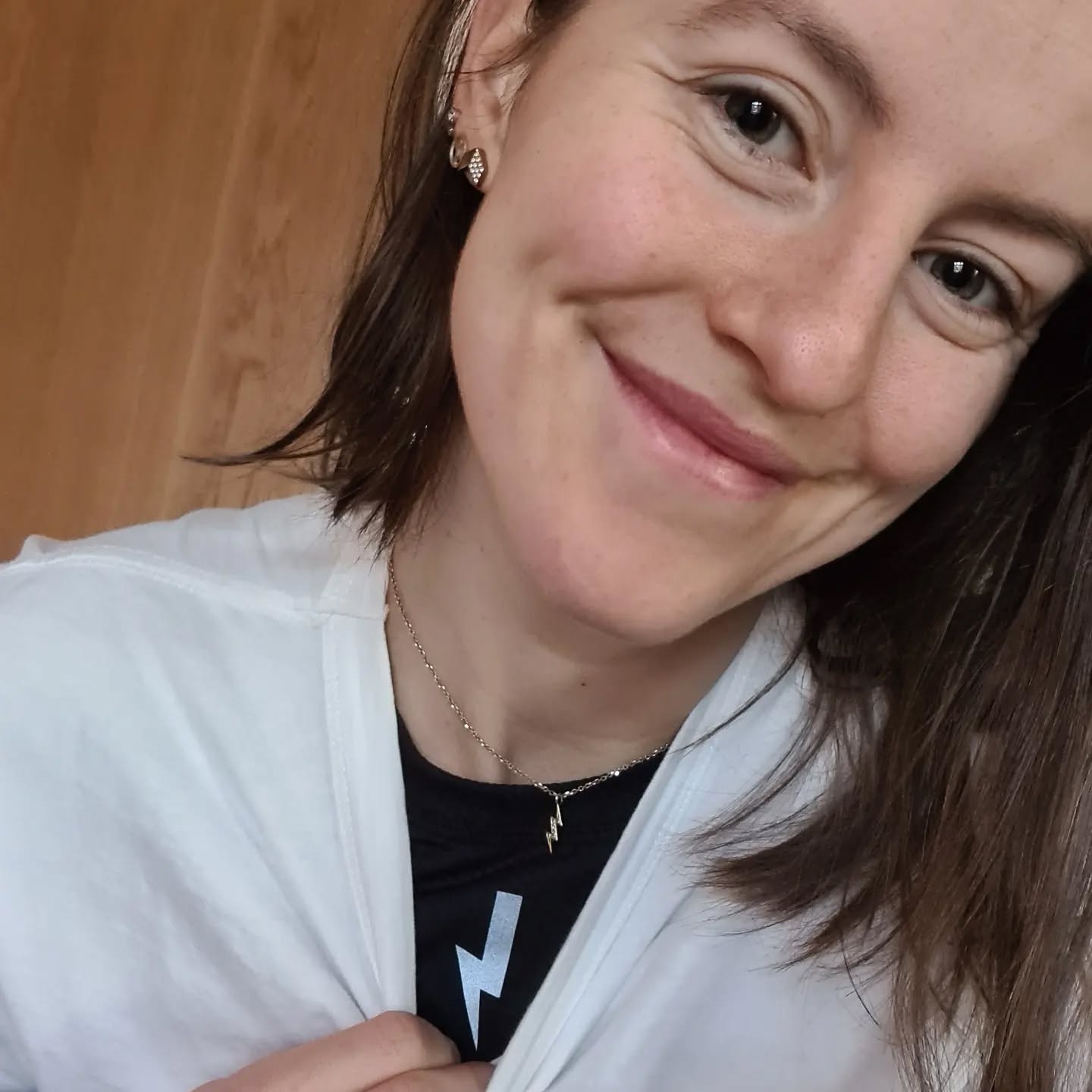 Close-up-of-a-smiling-woman- wearing-a-white-shirt-a-black-shirt- with-a-lightning-bolt-logo-and-a- small-silver-lightning-bolt-necklace