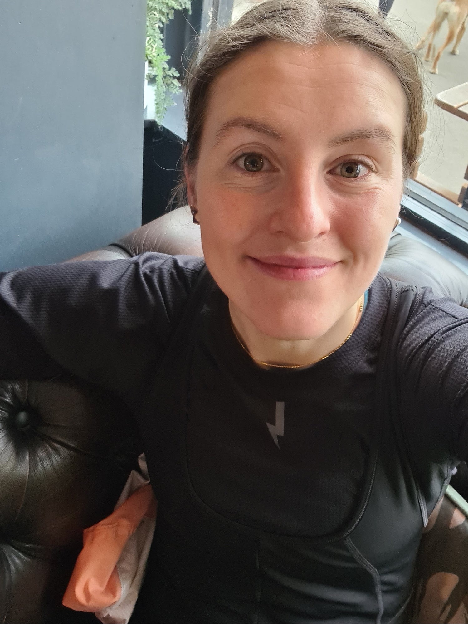 Young-woman-wearing-a-black- long-sleeve-athletic-top-sitting-on-a-brown-leather-couch-indoors