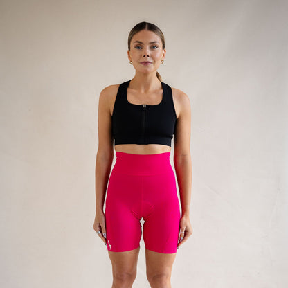 Front view of a woman model wearing the LUCA women's high-waisted padded cycling shorts in hot pink, paired with a black front-zip sports bra against a neutral studio backdrop Empower Short