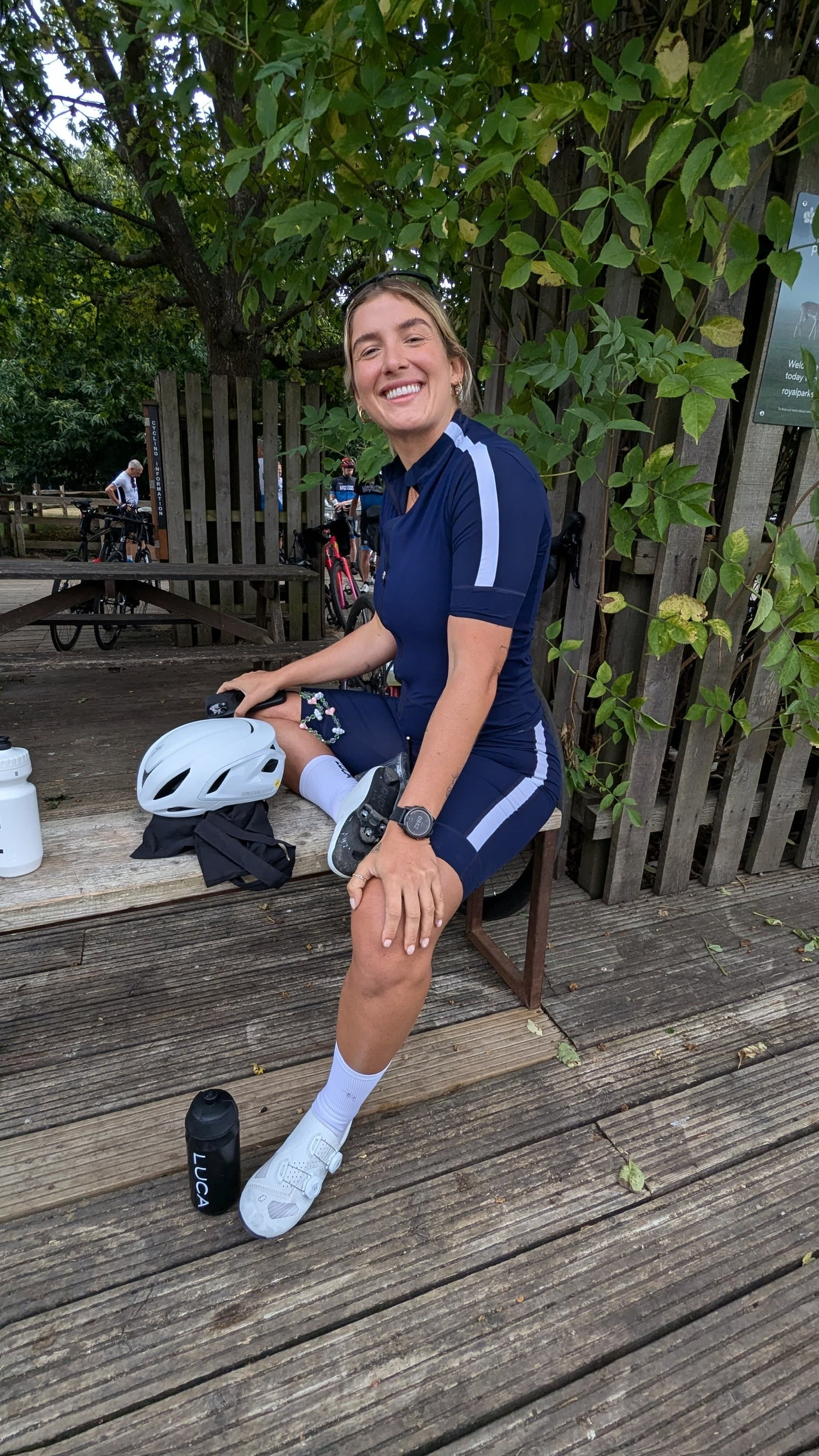 Smiling-female-cyclist-in-a-dark-blue-and-white-cycling-jersey-and- matching-shorts-sitting-outdoors-on-a-wooden-deck