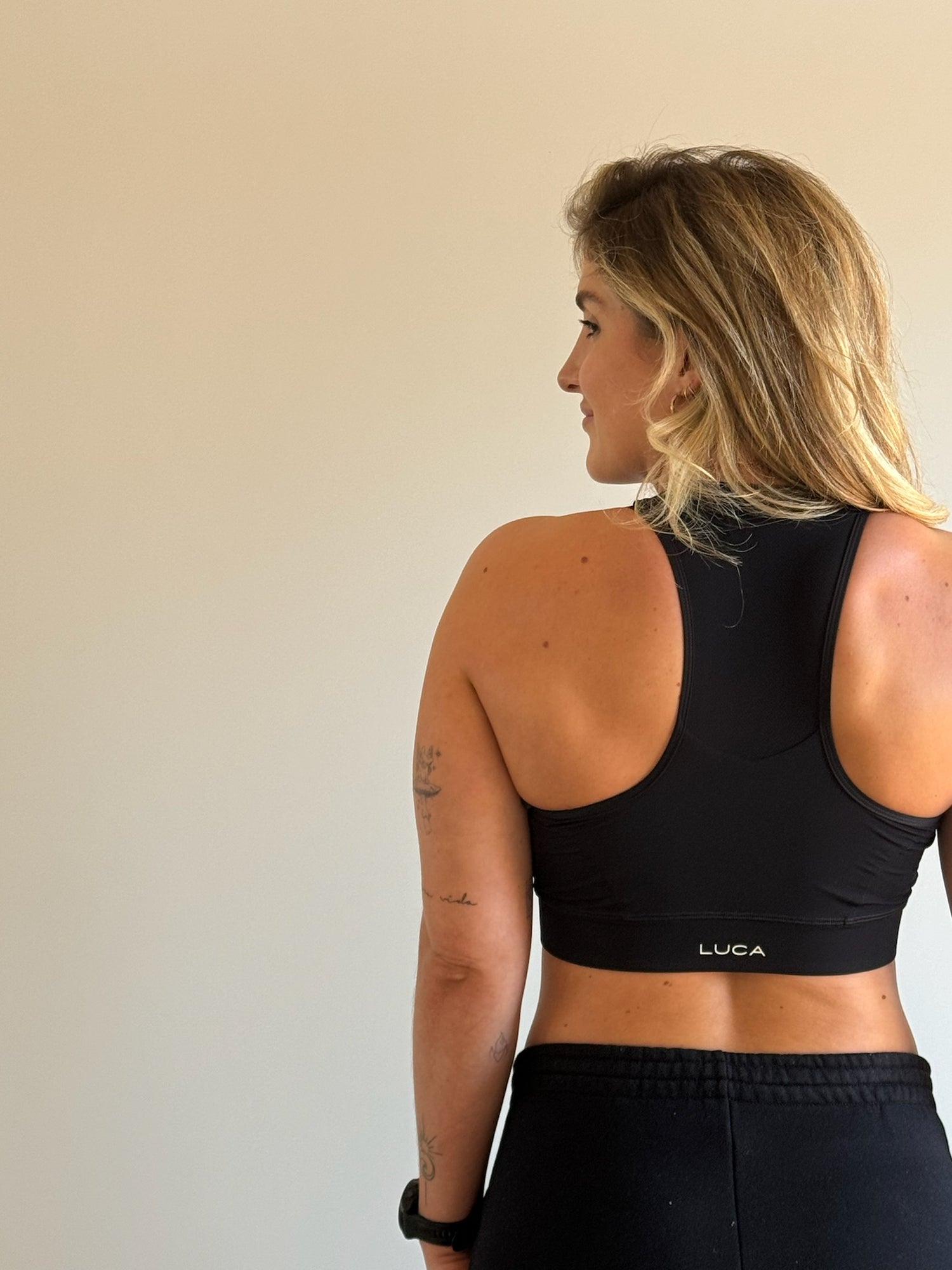 Rear-view-of-a-blonde-woman- wearing-a-black-high-neck-sports- bra-with-a-white-logo-detail-on-the- band