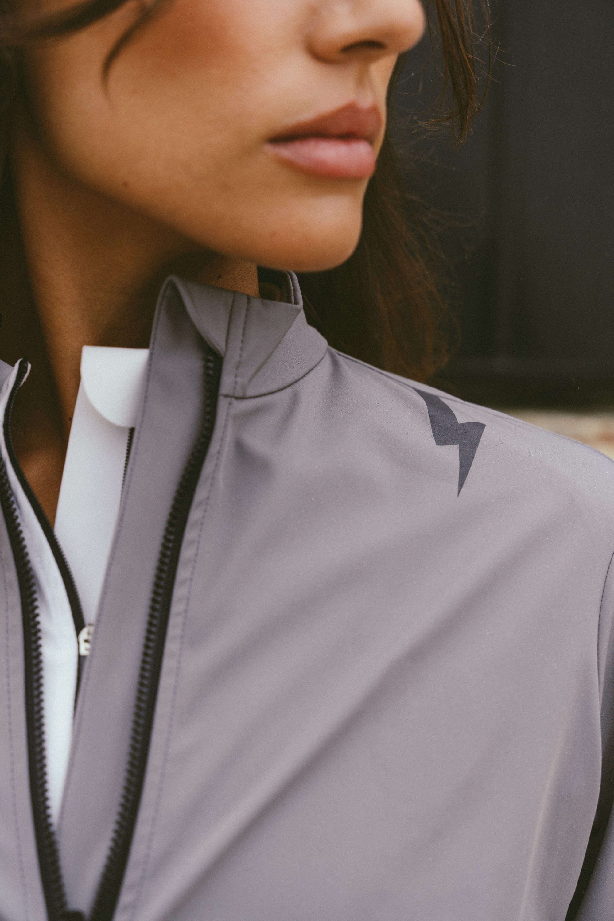 Detail-shot-of-the-high-collar-and- shoulder-of-a-light-grey- performance-jacket-The-jacket-is- slightly-unzipped-revealing-a-white- collar-underneath-The-dark-grey- stylized-lightning-bolt-sign-is-visible-on the-upper-shoulder-area