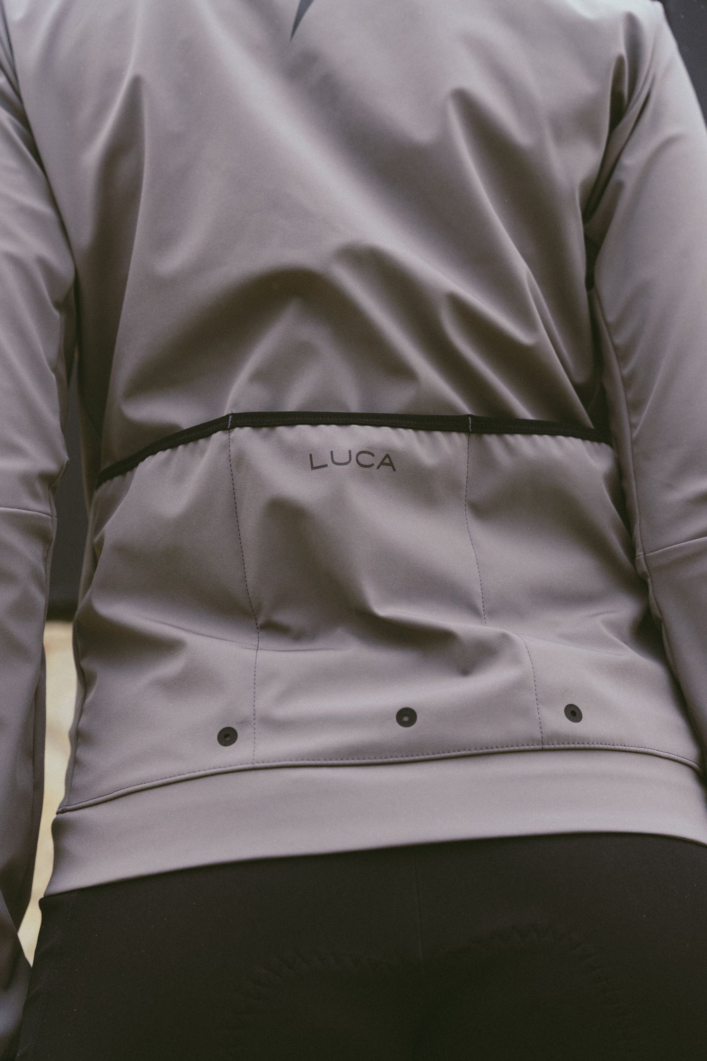 Back-view-of-the-taupe-grey-Luca-cycling-jacket-the-LUCA-logo-and-the-vents-for-temperature-regulation-while-riding