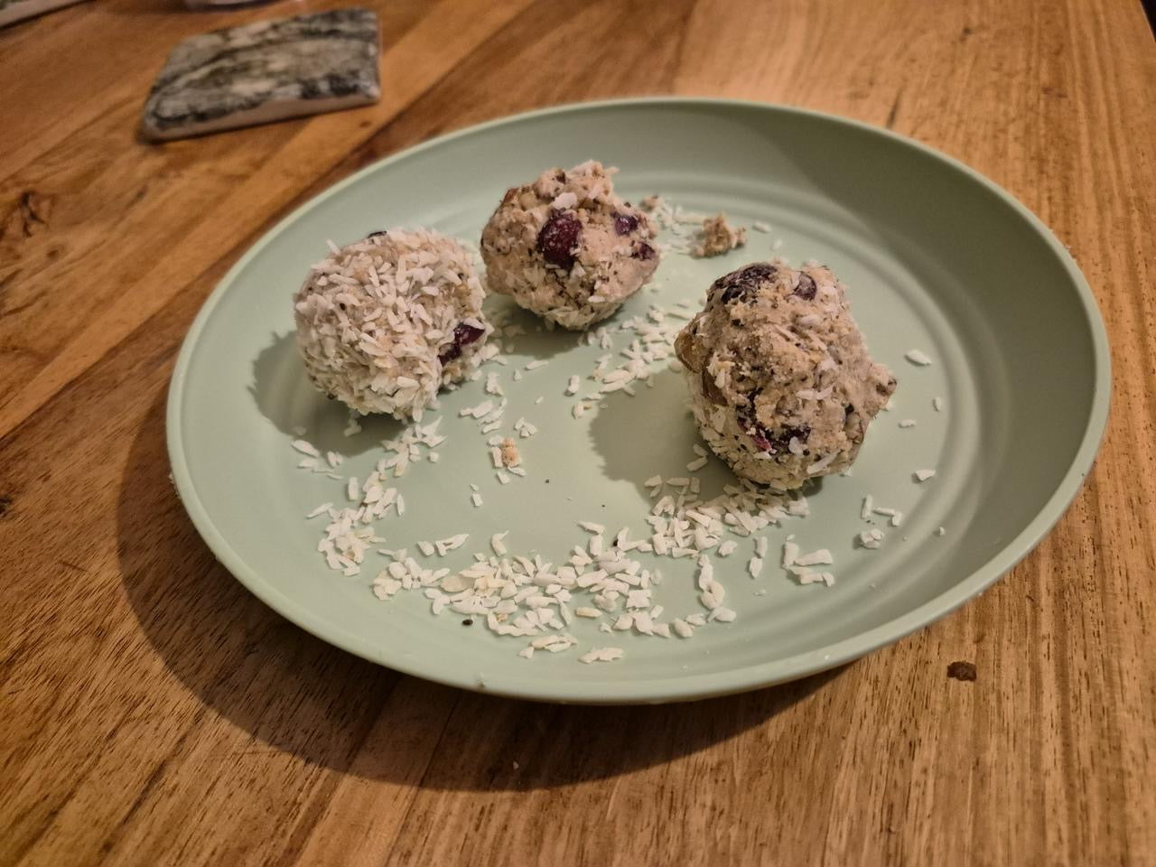 Three-homemade-unbaked-energy-balls-dough-portions-served-on-a- light-mint-green-plate-The-treats- contain-dried-fruit-(like-cranberries)-and-nuts-and-one-is- rolled-in-shredded-coconut-flakes- scattered-lightly-across-the-plate