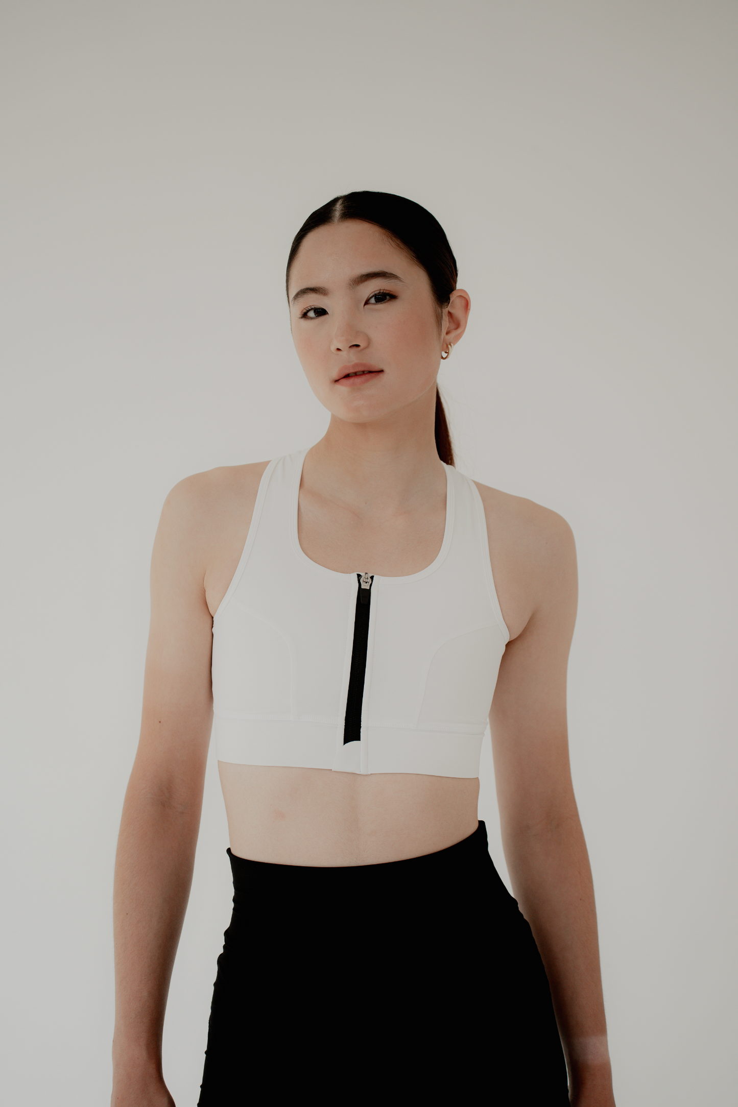 A-flattering-straight-on-photo-of-a- woman-modeling-the-off-white-sports- bra-with-a-contrast-black-front-zipper- The-bra-features-thick-shoulder-straps-and-a-wide-support-band-She- is-also-wearing-black-shorts-against-a-clean-minimalist-white-background- focusing-attention-on-the-sleek- functional-design-of-the-top