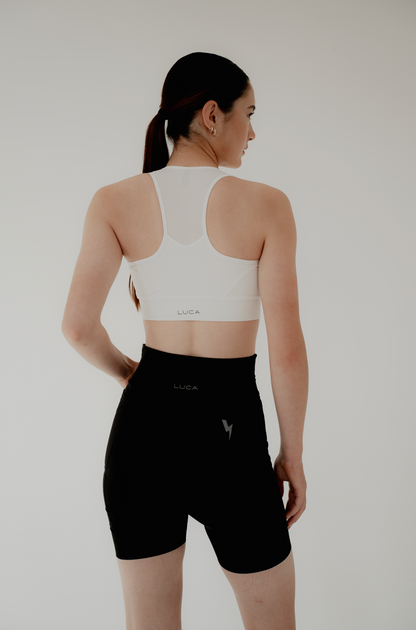 Back-view-of-a-woman-modeling-a-white-spots-bra-with-mesh-panel-and-LUCA-logo-paired-printed-with-black-high-waisted-biker-shorts-featuring-a-reflective-lighting-bolt-graphic