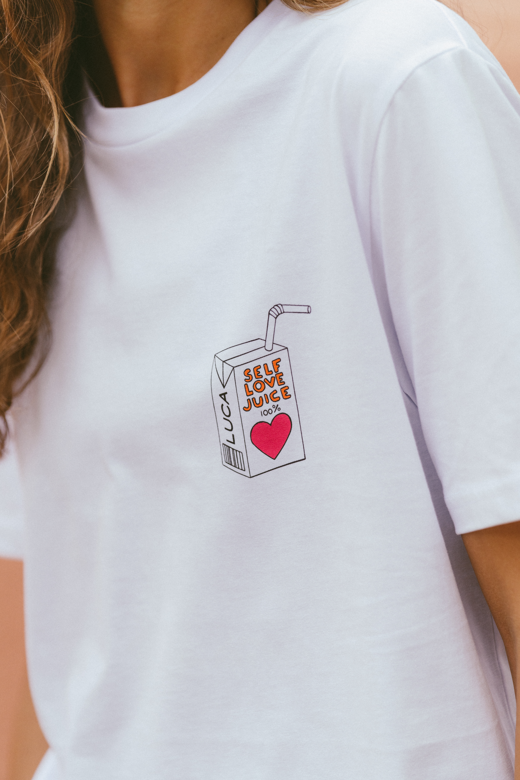 Close-up-of-a white-Self-Love-Juice-t-shirt-with-a-heart-and-straw-graphic-embroidered-on-the- pocket-area