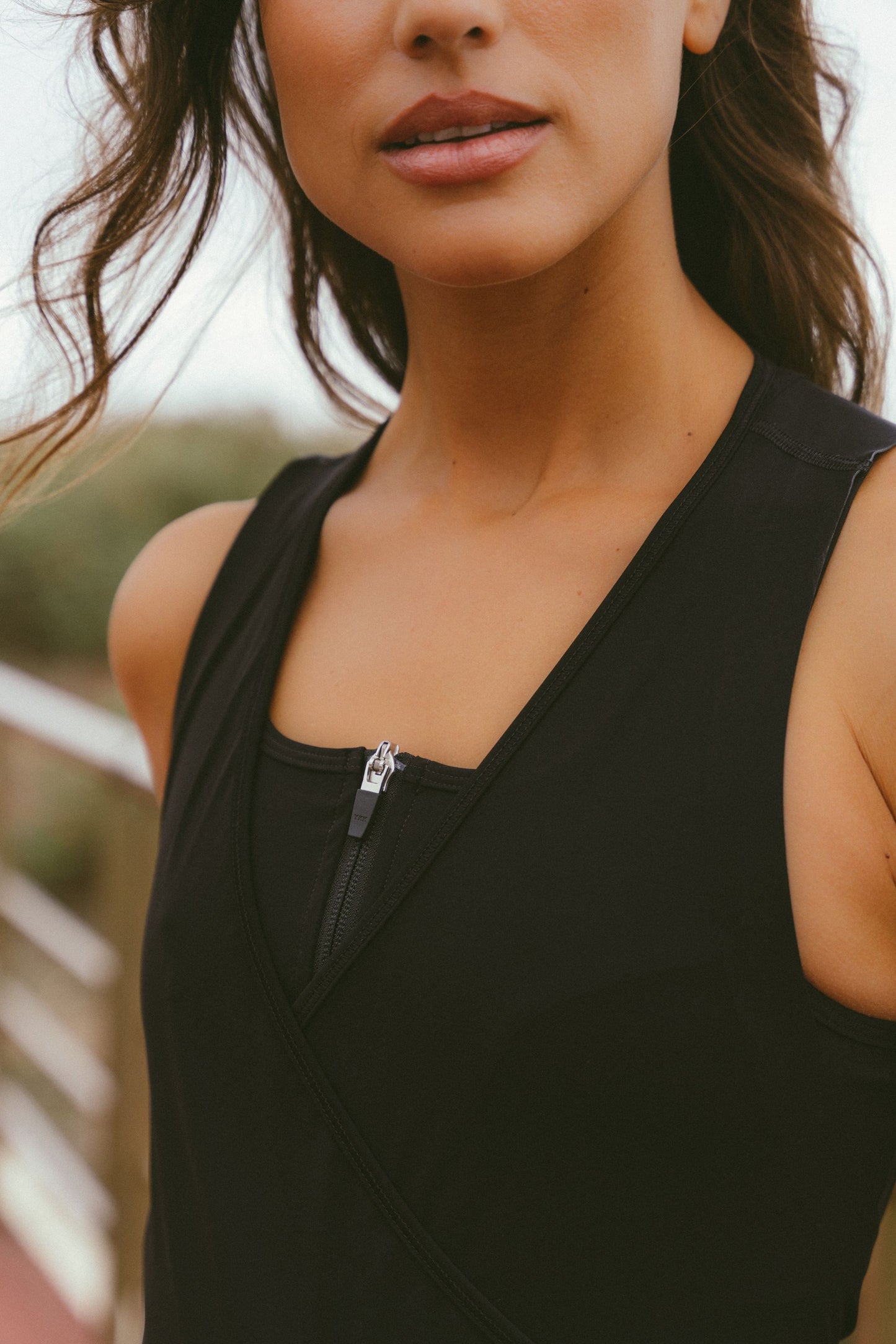 Extreme-close-up-shot-focusing-on- the-neckline-of-a-black-athletic- cycling-garment-showing-the-detail- of-a-silver-zipper-pull-at-the-center- of-the-chest-The-garment-features-a-V-neck-overlapping-design-over-a-high-neck-inner-layer-The-model's-chin-and-mouth-are- partially-visible-in-the-top-of-the- frame