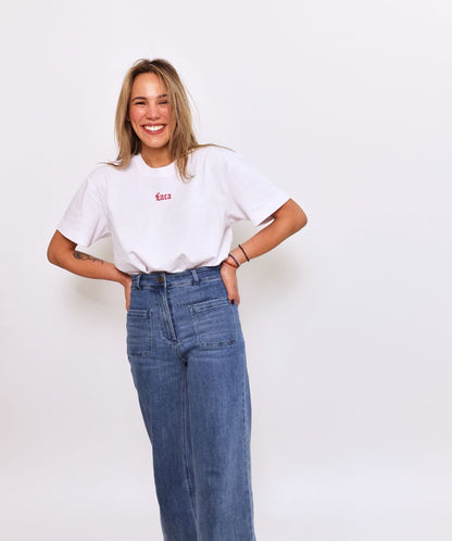Smiling-model-wearing-a-white-Luca-logo-t-shirt-with-a-small-red- script-logo-and-wide-leg-denim-jeans