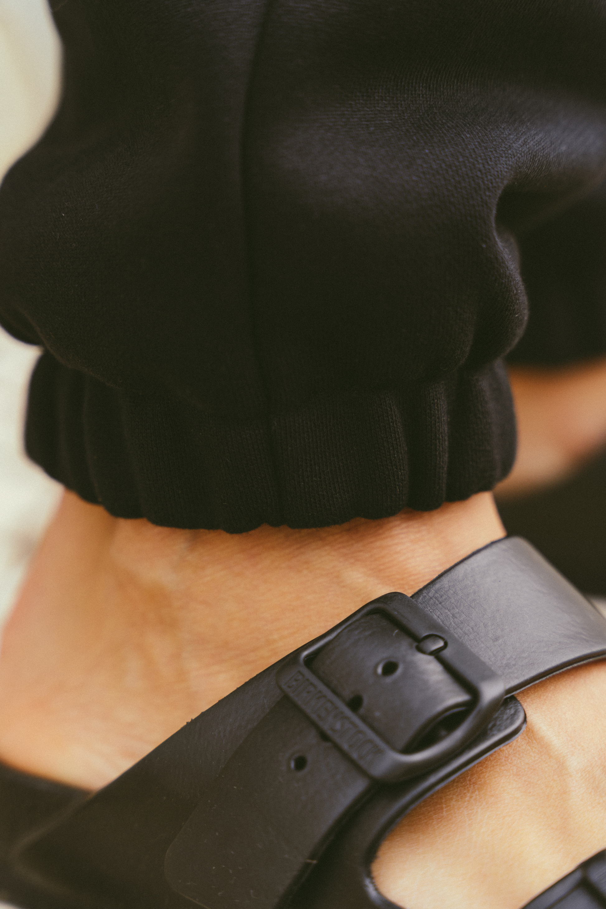 Close-up-of-a-person-wearing-black-joggers-with-elastic-cuffs-paired-with-black-birkenstock-sandals