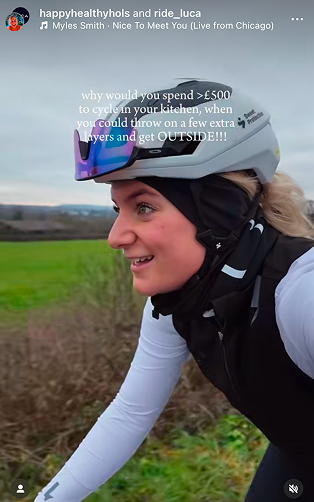 Close-up-of-a-smiling-female-cyclist- riding-outdoors-She-is-wearing-layered-winter-cycling-gear-a-white- long-sleeve-jersey-a-black-vest-a- black-neck-gaiter-and-a-light-gray- helmet-with-mirrored-sunglasses-The- text-overlay-asks-why-would-you- spend->£500-to-cycle-in-your-kitchen-when-you- could-throw-on-a-few-extra-layers- and-get-OUTSIDE