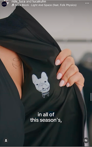 Detail-shot-of-a-woman's-hand-holding-open-the-inner-lining-of-a- black-technical-jacket-A-custom- graphic-featuring-a-French-Bulldog- wearing-a-cycling-jersey-collar-along-with-a-handwritten-signature- is-visible-on-the-inner-panel