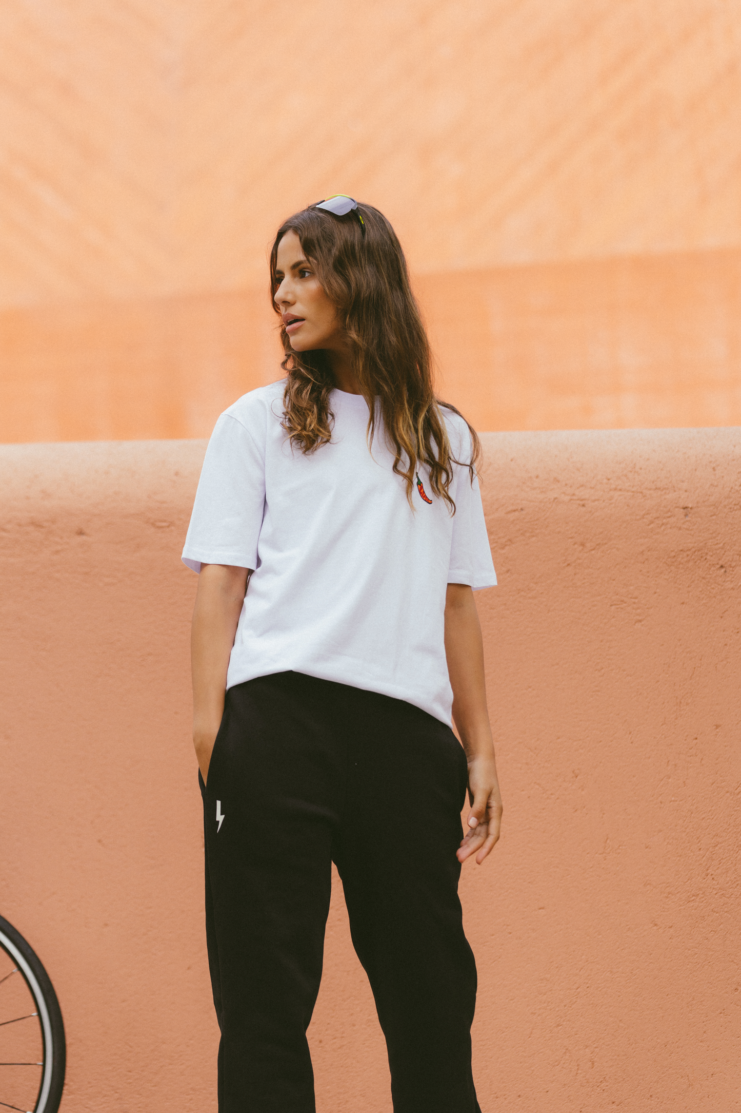 Stylish-woman-wearing-black-lighting-bolt-sign-joggers-paired-with-a-simple-oversized-white-t-shirt-for-a-chic-casual-and-comfortable-athleisure-look-against-a-warm-terracotta-wall