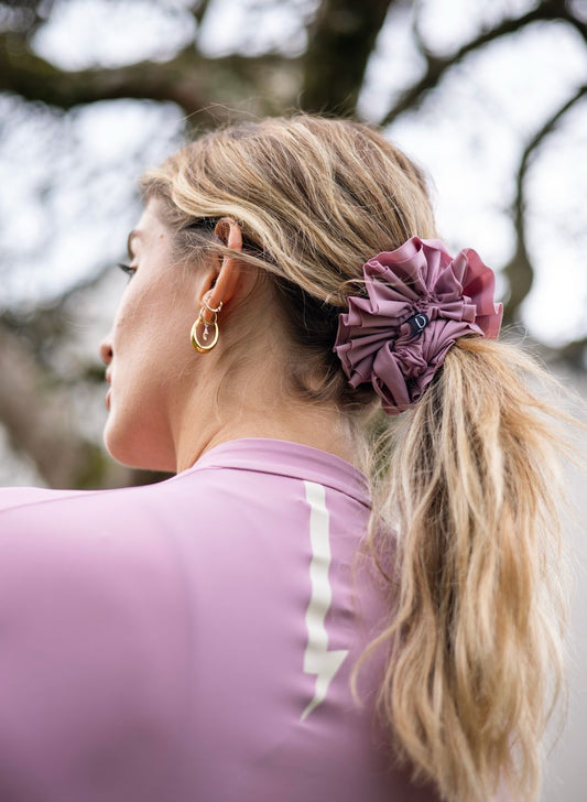 Woman-with-a-blonde-ponytail- secured-by-a-dusty-rose-ruffled- scrunchie-wearing-a-matching-long-sleeve-top-with-a-lightning-bolt-sign