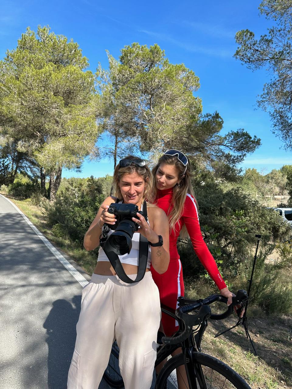 Two-women-outdoors-one-taking-a- picture-with-a-professional-camera- and-the-other-standing-next-to-a- bicycle