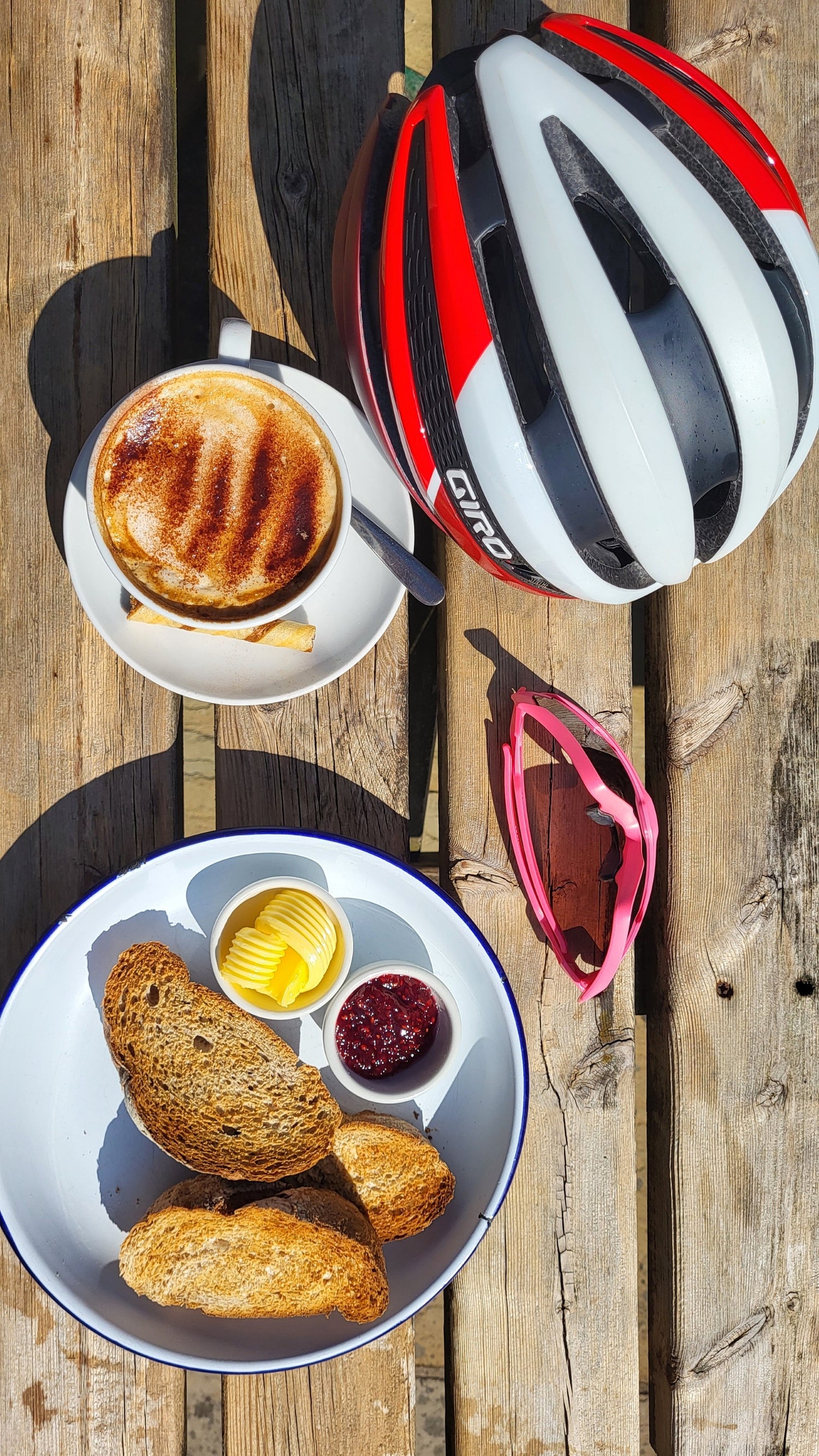 Cycling-helmet-and-pink-sunglasses-resting-on-a-wooden- table-next-to-a-cup-of-coffee-and- toast-symbolizing-a-mid-ride- refueling-stop