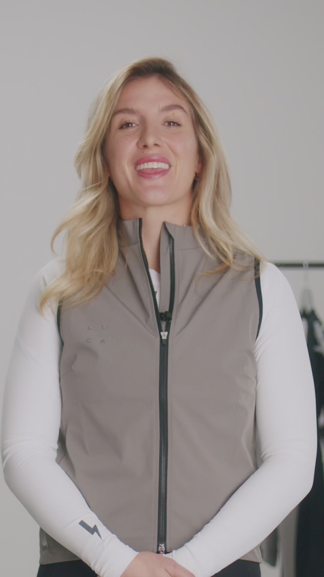 Video-demonstrating-the-features-of-the-Luca-Ascend-cycling-gilet-in-taupe-color-A-women-details-the-gilet-three-layer-windproof-and-water-repellemt-faric-moisture-wicking-inner-layer-doule-ended-zipper-silicone-gripper-hem-reflective-logos-and-the-ergonomic-cut-for-riding-comfort