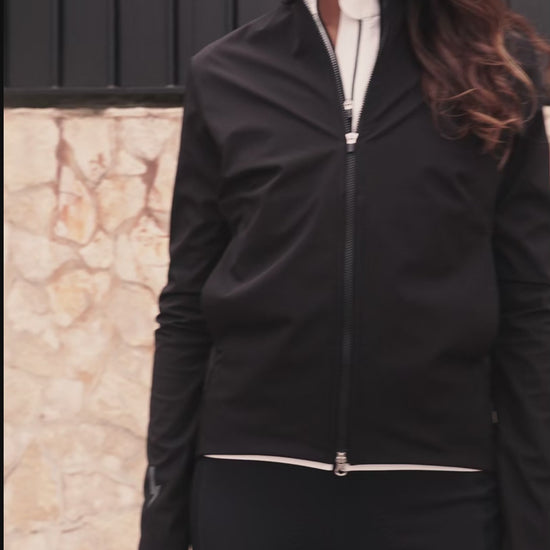 Video-thumbnail-showing-a-women-modeling-the-Black-Momentum-jacket-zipping-it-up-and-turning-to-reveal-the-reflective-lighting-bolt-sign-and-LUCA-branding-on-the-back-while-walking-outdoors