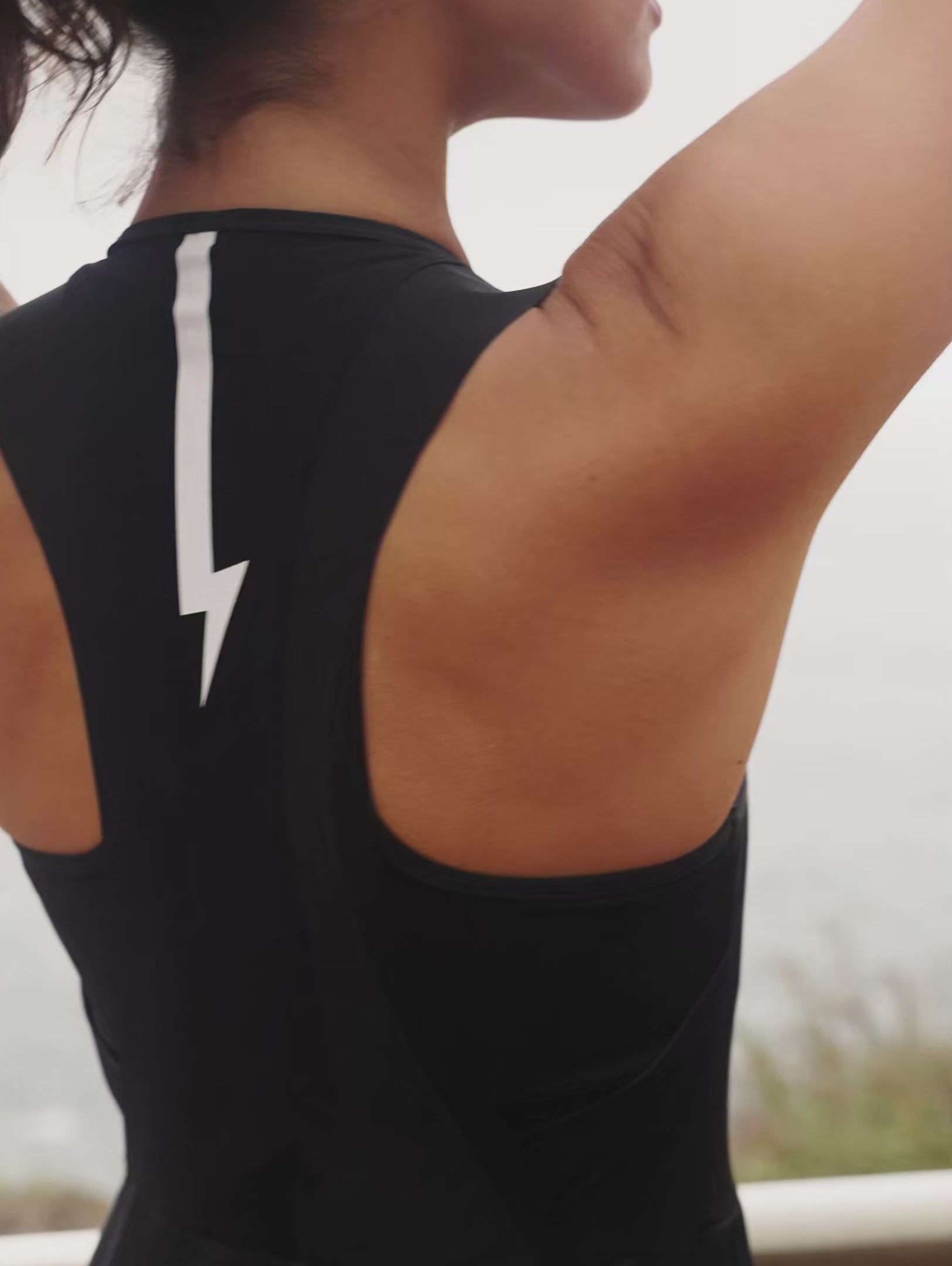 Short-video-demonstrating-the-fit-of-a-black-sleeveless-athletic-one-piece-  with-cycling-short-legs-a-square- neckline-and-a-contrasting-white- lightning-bolt-sign-on-the-upper-back