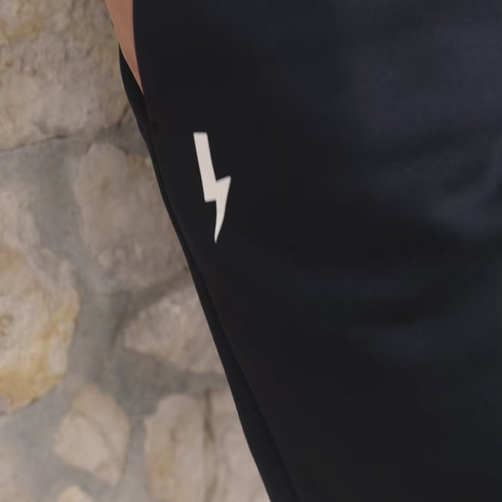 A-close-up-video-showcasing-a-model-wearing-a-black-long-sleeve-athletic-base-layer-shirt-and-matching-black-fleece-joggers-The-top-features-a-subtle-textured-and-a-small-lighting-bolt-sign-on-the-chest-The-model-puts-her-hands-in-the-deep-pockets-of-the-pents-demonstrating-the-comfort-fit-and-the-white-lighting-bolt-logo-on-the-thigh-This-highlights-the-versatility-of-the-high-quality-monochromatic-workout