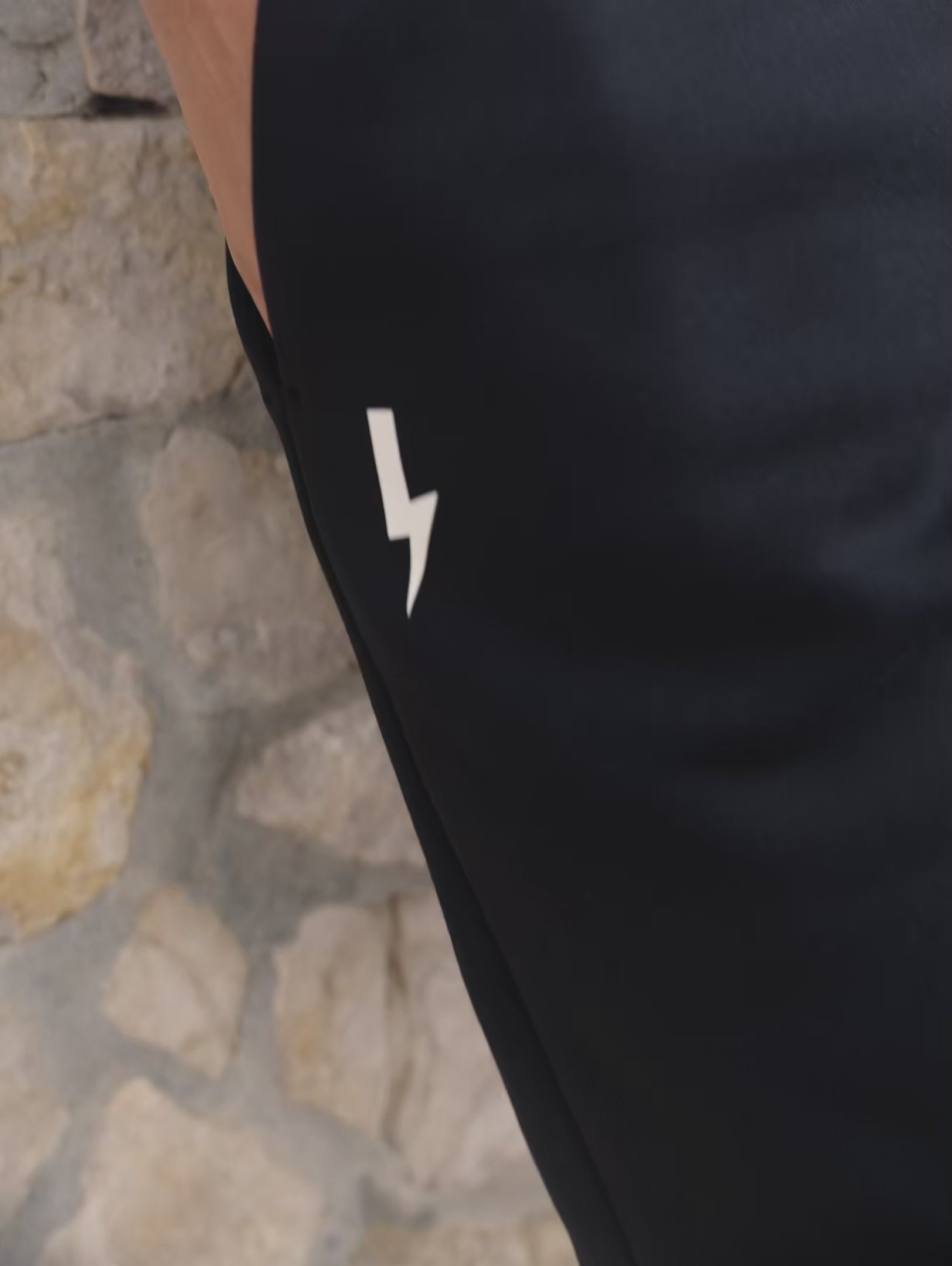 A-close-up-video-showcasing-a-model-wearing-a-black-long-sleeve-athletic-base-layer-shirt-and-matching-black-fleece-joggers-The-top-features-a-subtle-textured-and-a-small-lighting-bolt-sign-on-the-chest-The-model-puts-her-hands-in-the-deep-pockets-of-the-pents-demonstrating-the-comfort-fit-and-the-white-lighting-bolt-logo-on-the-thigh-This-highlights-the-versatility-of-the-high-quality-monochromatic-workout